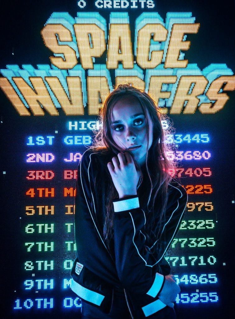 woman posing for photo in front of Space Invaders scoreboard